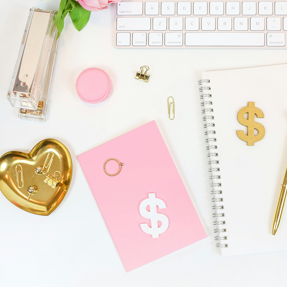 Flachlay mit rosa Notizbuch, weißem Notizblock, goldenen Büroclips und Tastatur – feminine Business-Desk-Szene.